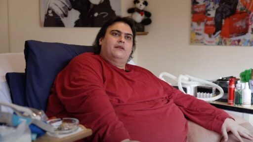 Jason Holton, Britain's fattest man, sitting on a bed