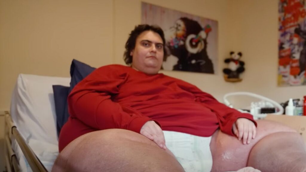 Jason Holton, Britain's fattest man, sitting on a bed