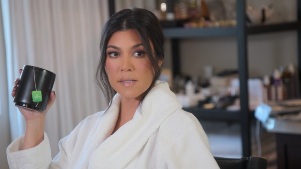 Kourtney Kardashian sits down getting her makeup done while wearing a white bath robe