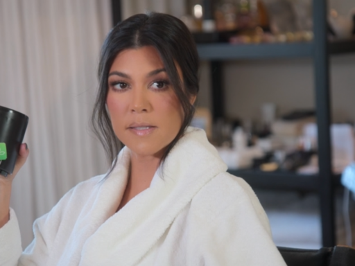 Kourtney Kardashian sits down getting her makeup done while wearing a white bath robe