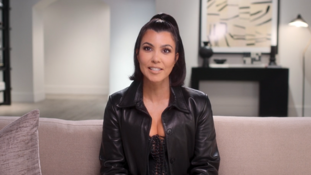 Kourtney Kardashian smiles while sitting down on a couch