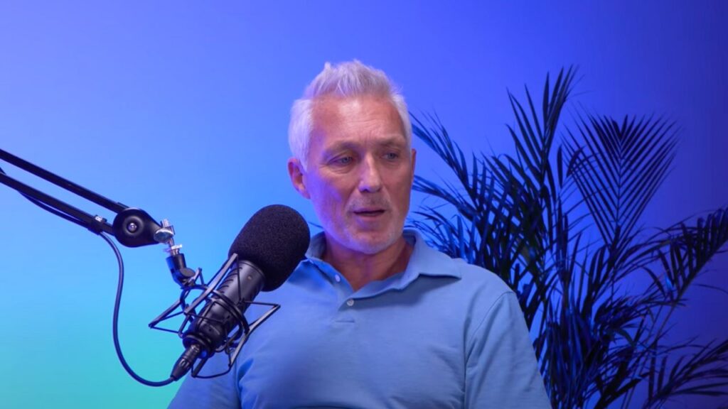 Martin Kemp sits next to a microphone wearing a blue shirt with a blue background