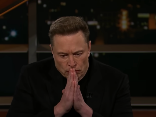 Elon Musk wears a black tee and blazer and sits in a chair