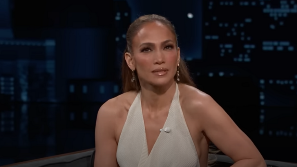 Jennifer Lopez wears a cream halterneck dress and sits on a couch