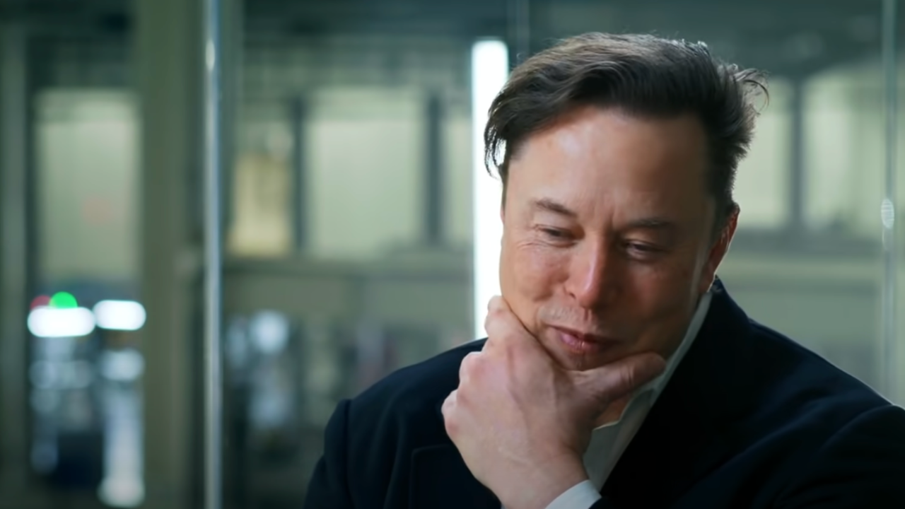 Elon Musk wears a white shirt and navy blazer