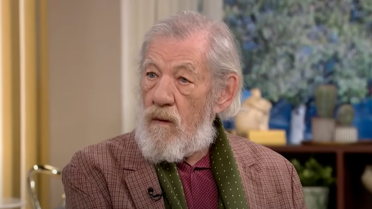 Sir Ian McKellen wears a paid jacket, green scarf and burgundy shirt