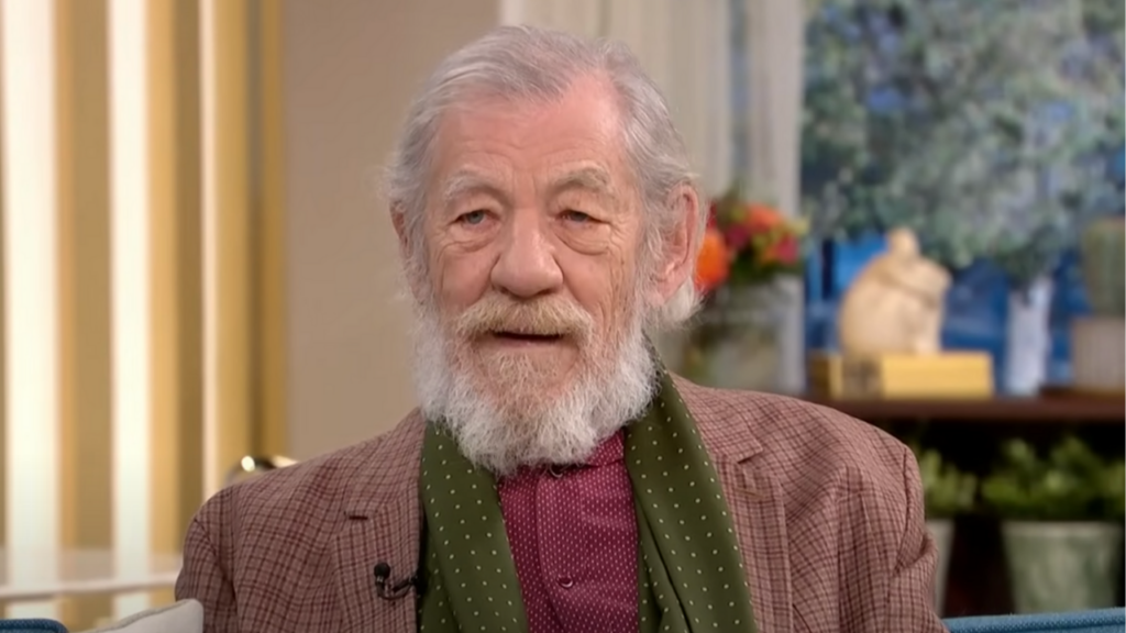 Sir Ian McKellen wears a paid jacket, green scarf and burgundy shirt