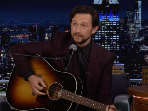 Joseph Gordon-Levitt wears a dark red suit, holds an acoustic guitar as he performs Lover by Taylor Swift