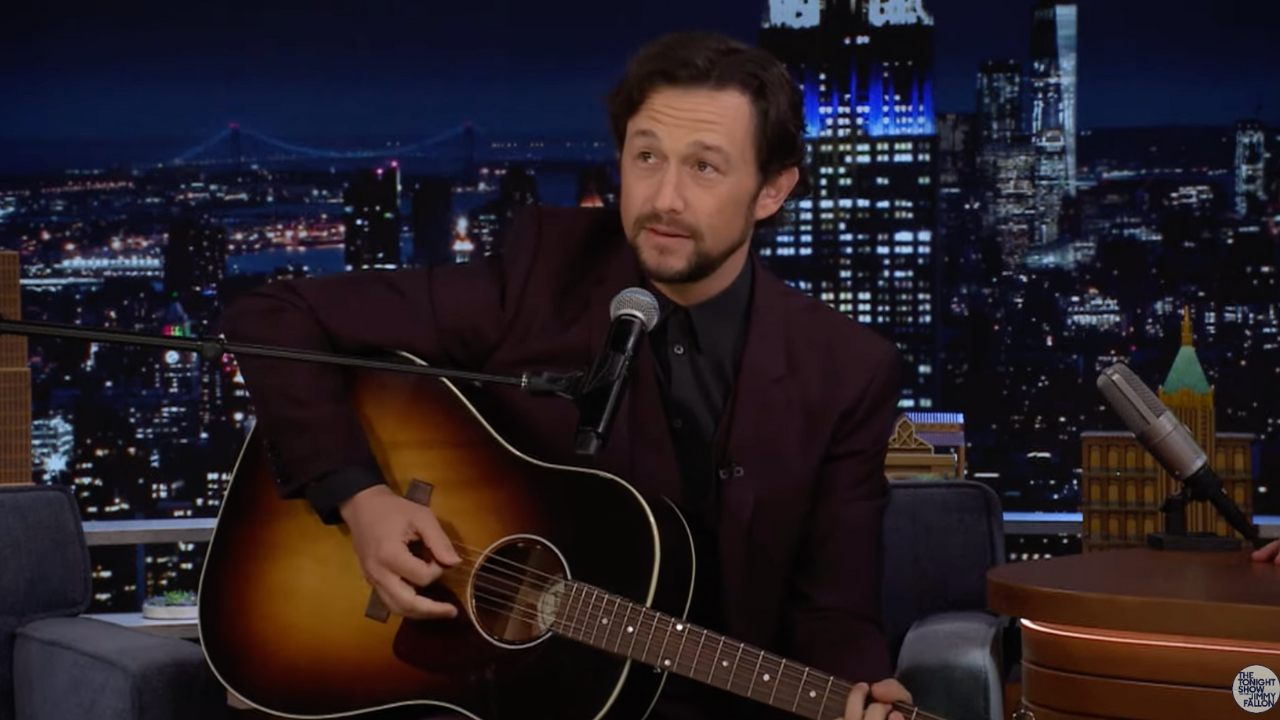 Joseph Gordon-Levitt wears a dark red suit, holds an acoustic guitar as he performs Lover by Taylor Swift