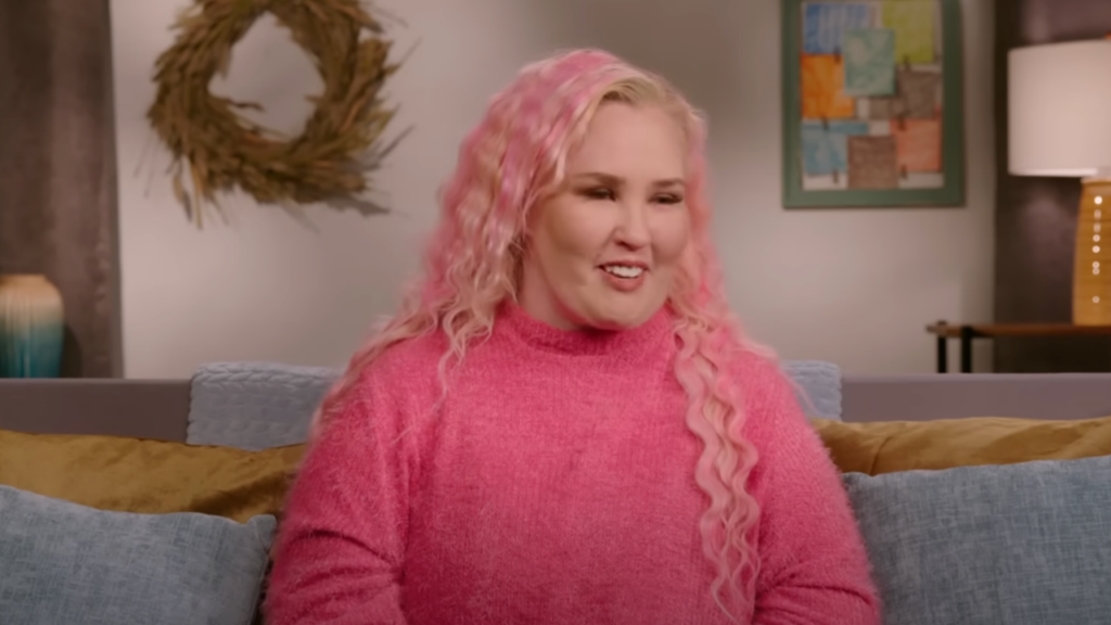 Mama June wears a pink jumper and sits on a gray couch